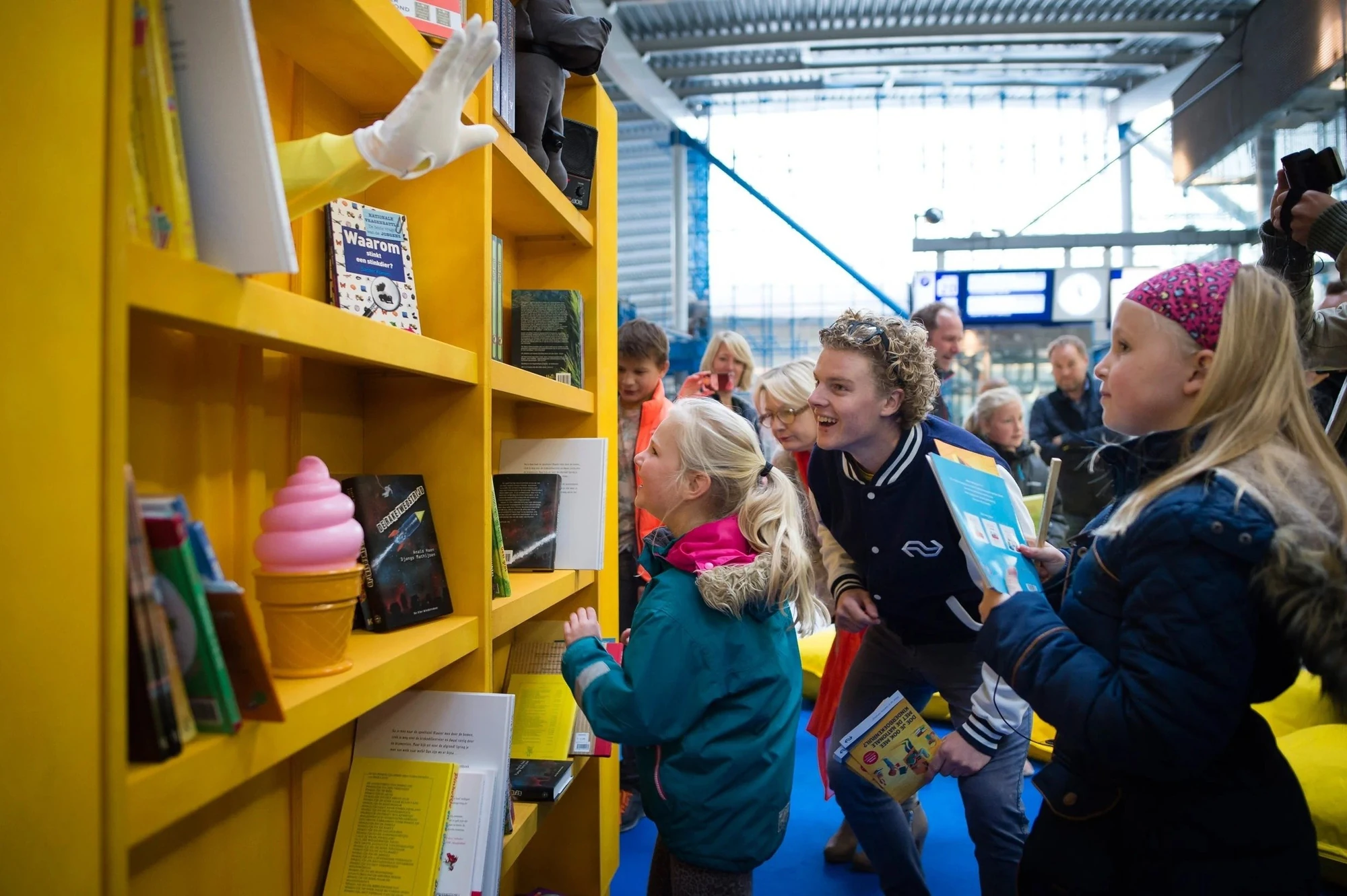 Levende boekenkast: een arm met witte handschoen steekt uit de kast en reikt kinderen een boek aan