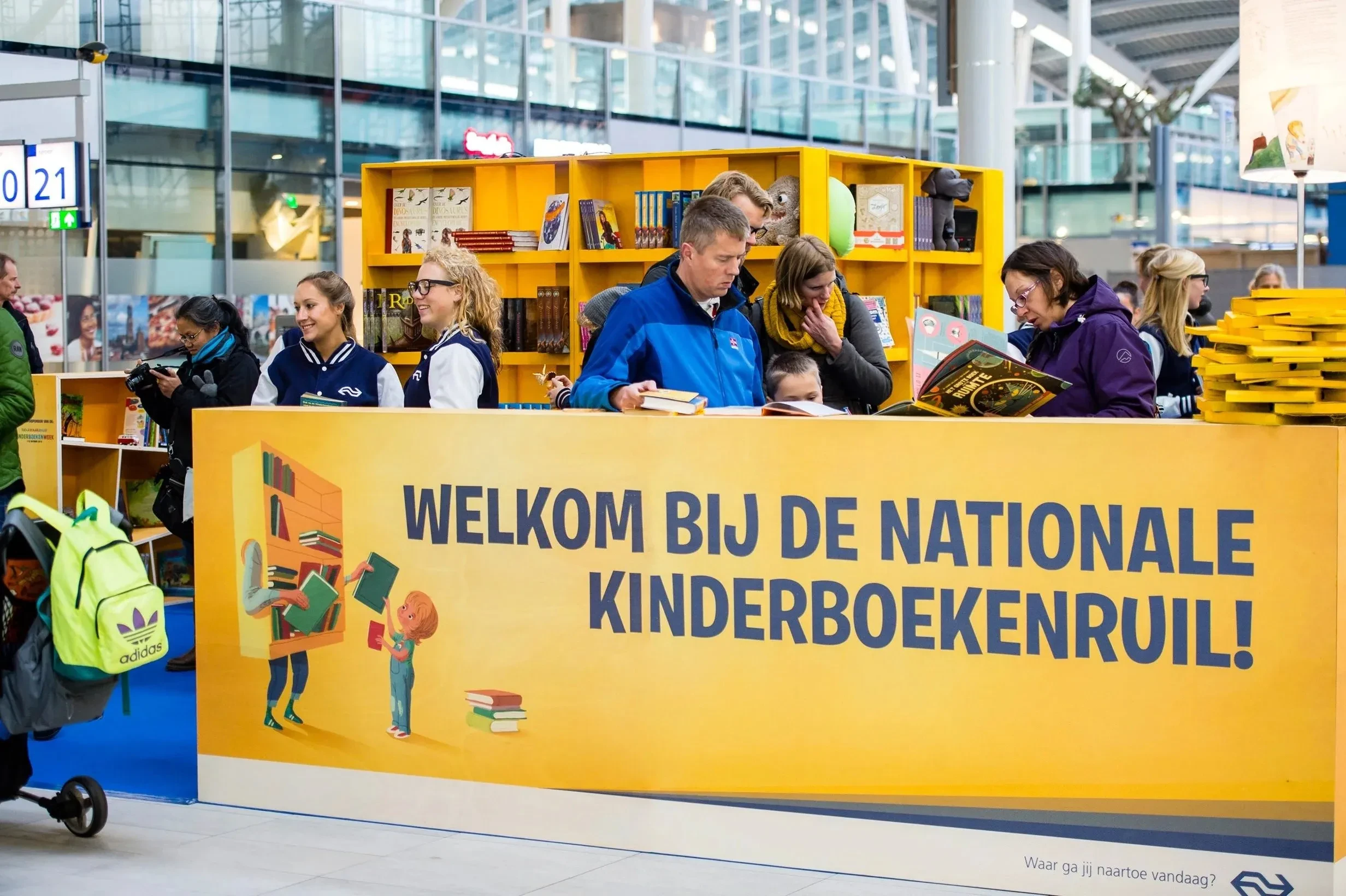 Gele stand van de NS Nationale Kinderboekenruil op Utrecht Centraal: ouders en kinderen kiezen boeken bij de welkomstbalie