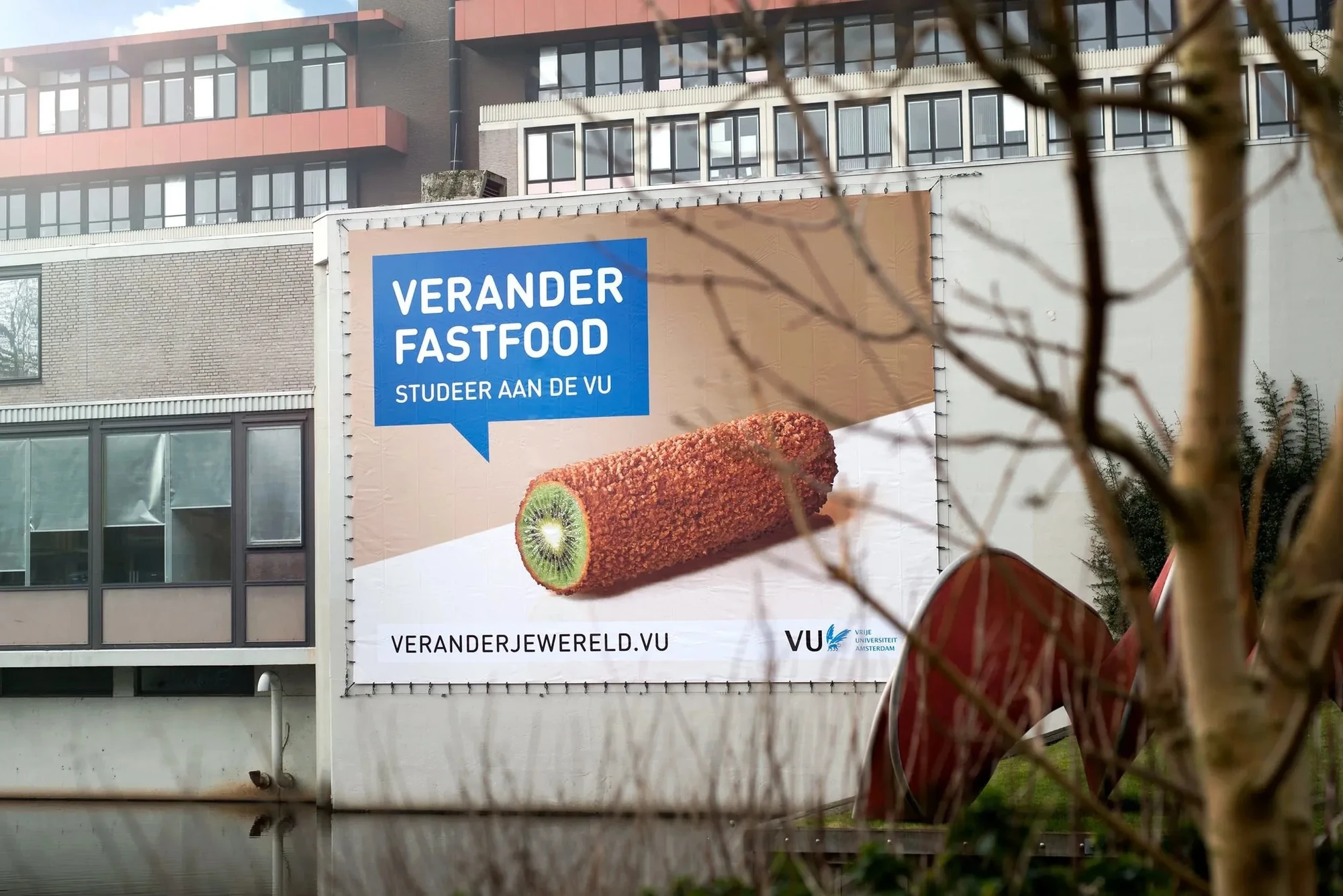 Spandoek op de VU-campus: "Verander fastfood. Studeer aan de VU", met een kiwi in de vorm van een frikandel